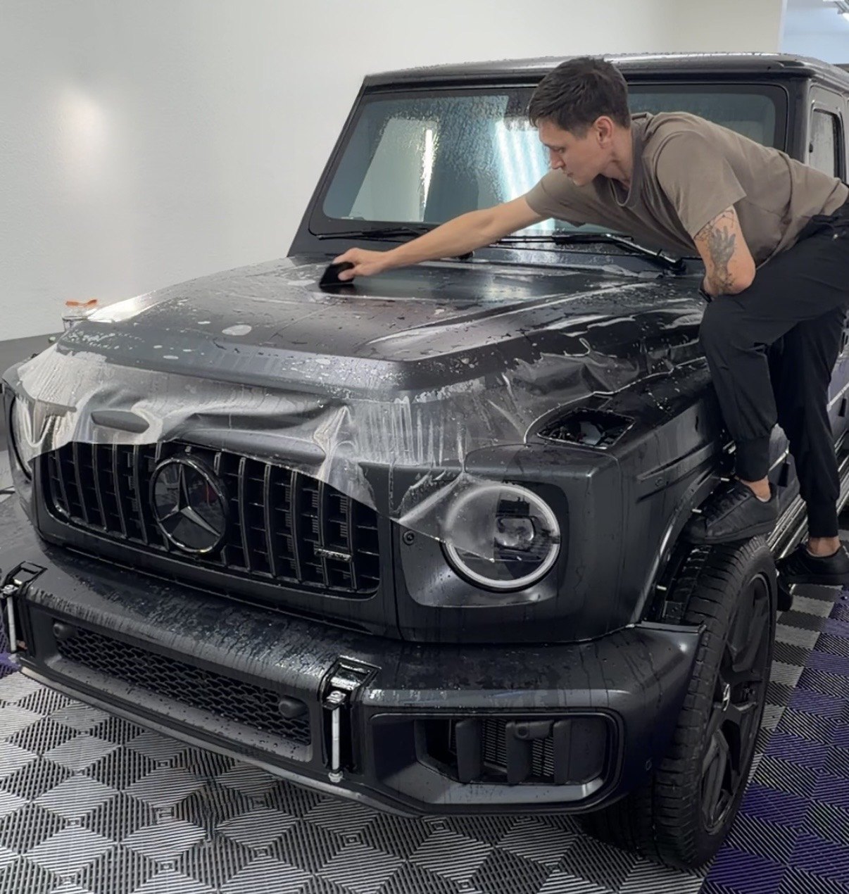 Clear film being laid across the hood of a black Mercedes G-Class